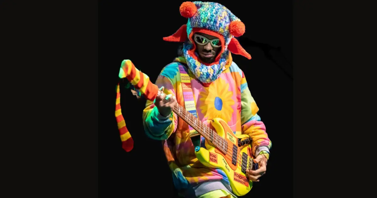 Mononeon sur scène avec sa basse sur laquelle pend une chaussette accrochée au bout du manche, ses habits sont de couleur vive.